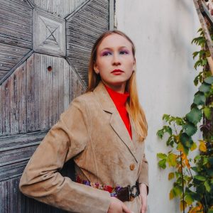 Femme en veste de daim fauve appuyee contre une vieille porte patinee dans la lumiere d automne