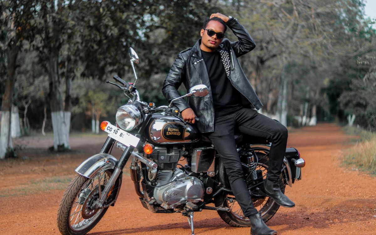 Buneri.fr | Bomber, motard ou racer : quel style de veste en cuir vous correspond ? Jeune homme posant avec une moto sur un chemin de terre, mettant en valeur une veste en cuir ajustée
