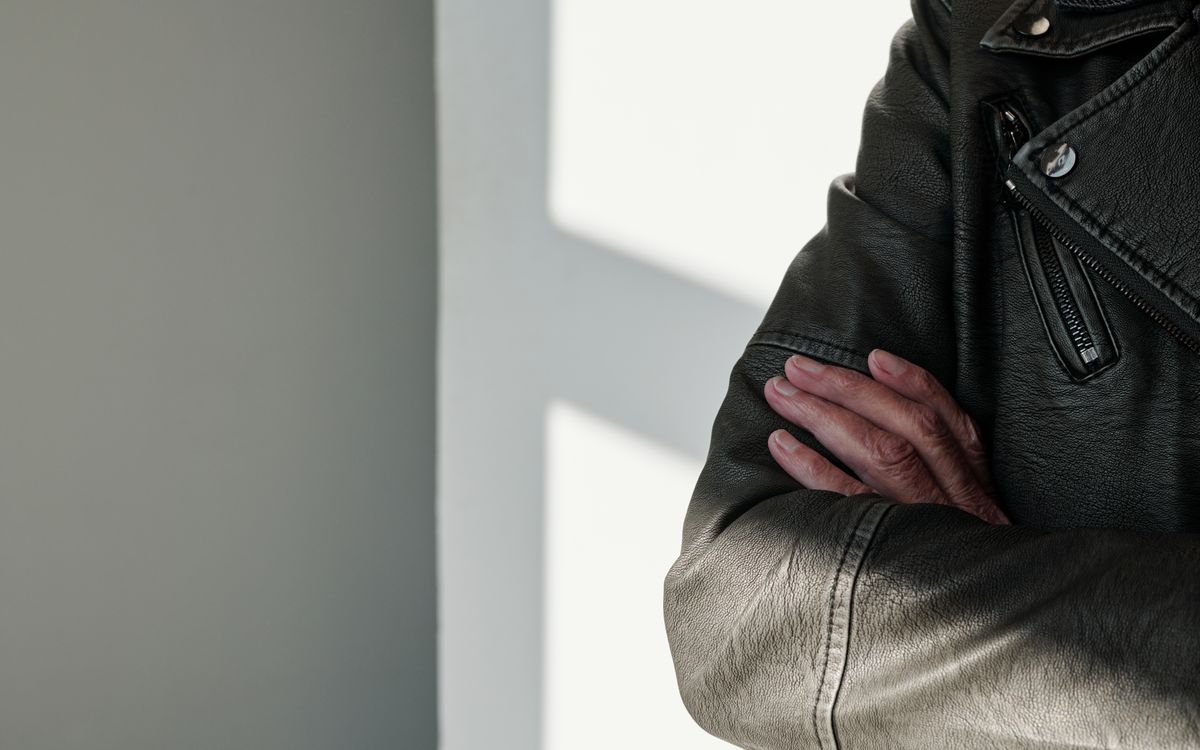 Gros plan sur des bras croises dans une veste en cuir noir sous une lumiere rasante