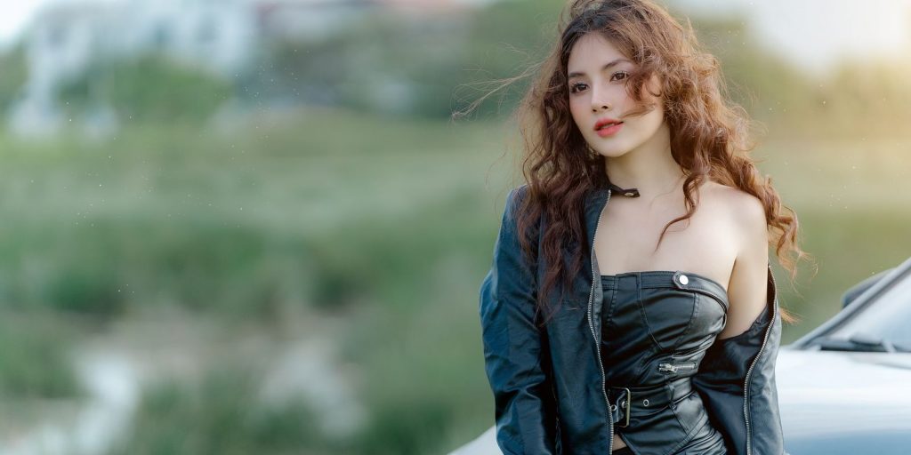 Jeune femme en veste de cuir posant avec assurance à l'extérieur près d'une voiture