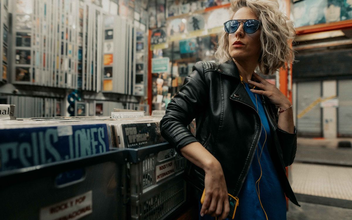 Femme élégante en veste de cuir et lunettes de soleil posant dans un magasin de vinyles