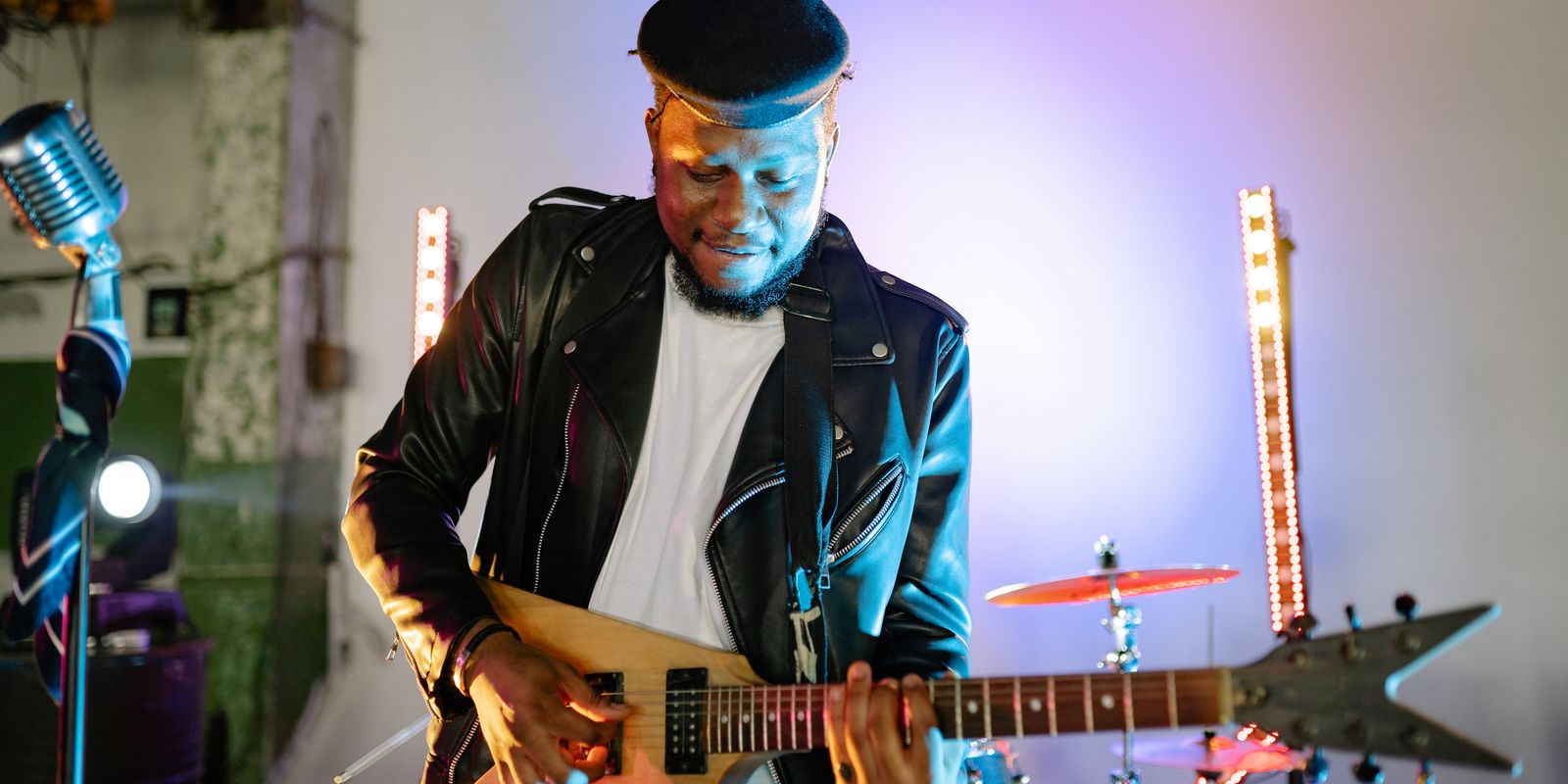 Buneri.fr | Pourquoi les PDG de la tech et les rock stars vivent en veste en cuir Guitariste jouant de la guitare électrique sur scène avec des lumières vives, portant une veste en cuir et une casquette plate