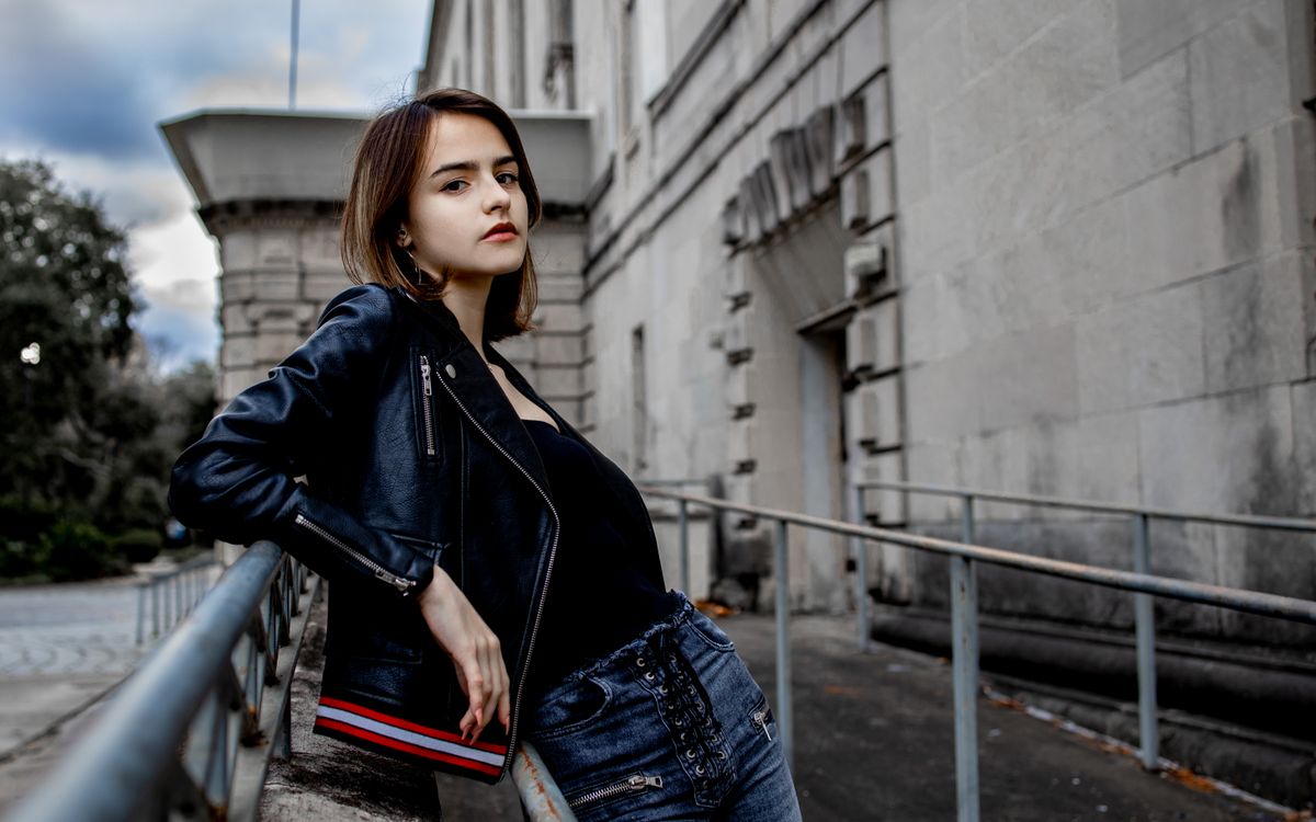 Jeune femme à la mode posant avec assurance en veste en cuir dans un décor urbain