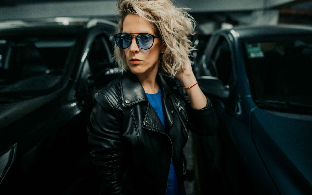 Buneri.fr | Que porter sous un blouson en cuir ? (Homme et femme) Femme élégante portant un blouson de cuir, posant avec assurance en milieu urbain