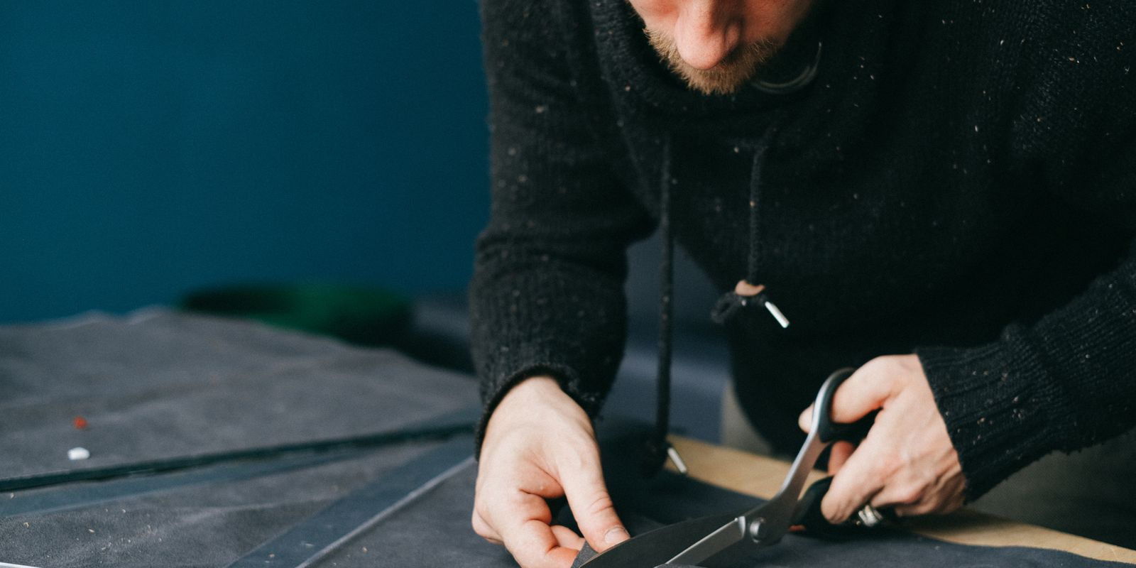 Buneri.fr | Réparer une veste en cuir : déchirures, éraflures et fermeture éclair Serious male tailor with scissors cutting circle out of leather material while standing at workbench in atelier