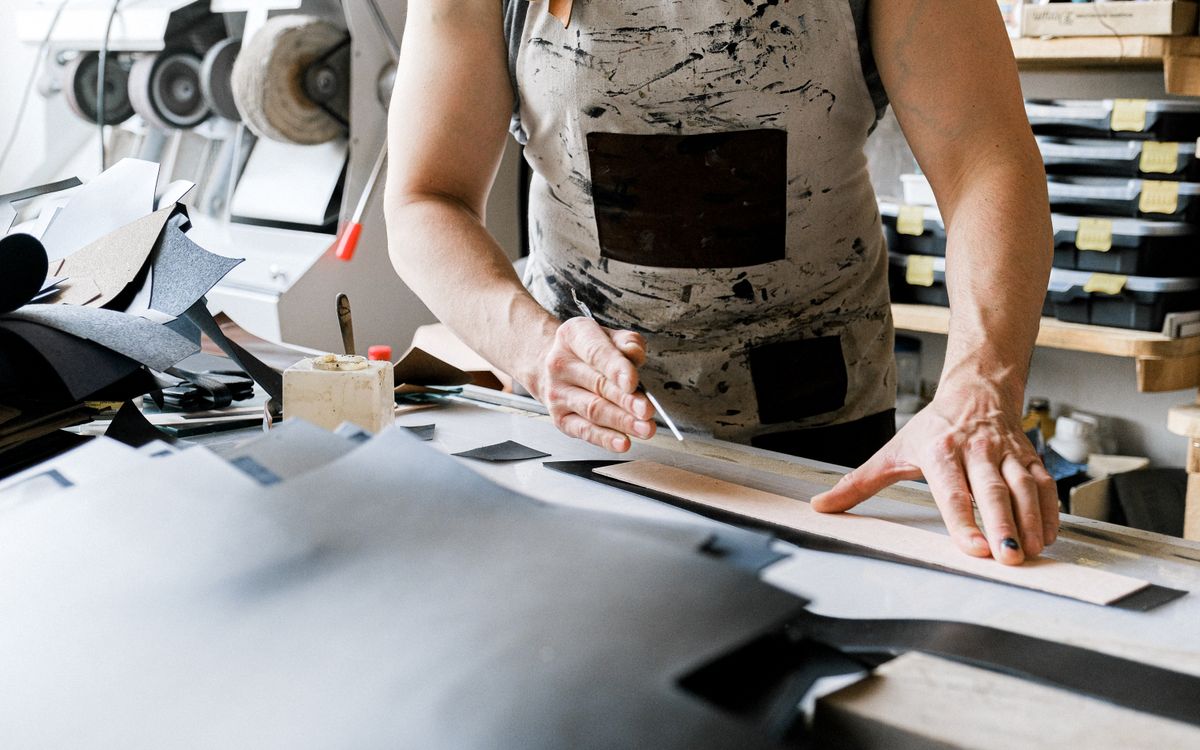 Buneri.fr | Réparer une veste en cuir : déchirures, éraflures et fermeture éclair A leather artisan actively crafting a piece in a well-equipped workshop, showcasing detailed handiwork