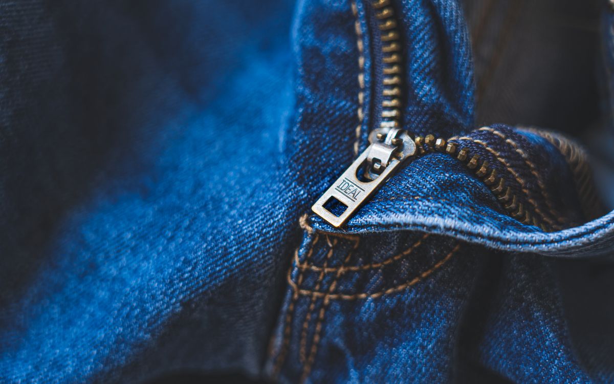 Buneri.fr | Réparer une veste en cuir : déchirures, éraflures et fermeture éclair Close-up of blue denim fabric featuring a metal zipper with detailed stitching