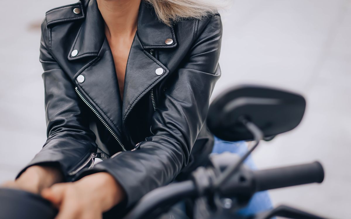 Gros plan d'une femme portant une veste en cuir noire à col montant sur une moto