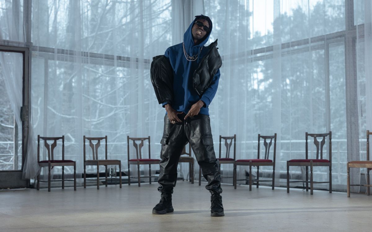 Buneri.fr | Veste en Cuir sur un Hoodie : Réussir le Streetwear Homme élégant en hoodie bleu et pantalon de cuir posant en intérieur avec un éclairage dramatique
