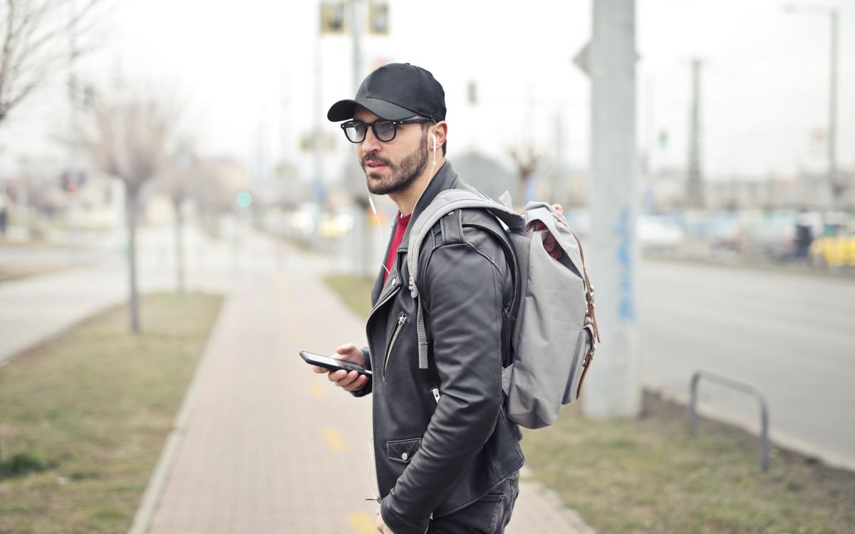 Buneri.fr | Veste en Cuir sur un Hoodie : Réussir le Streetwear Jeune homme élégant à Budapest consultant son smartphone dans une rue animée