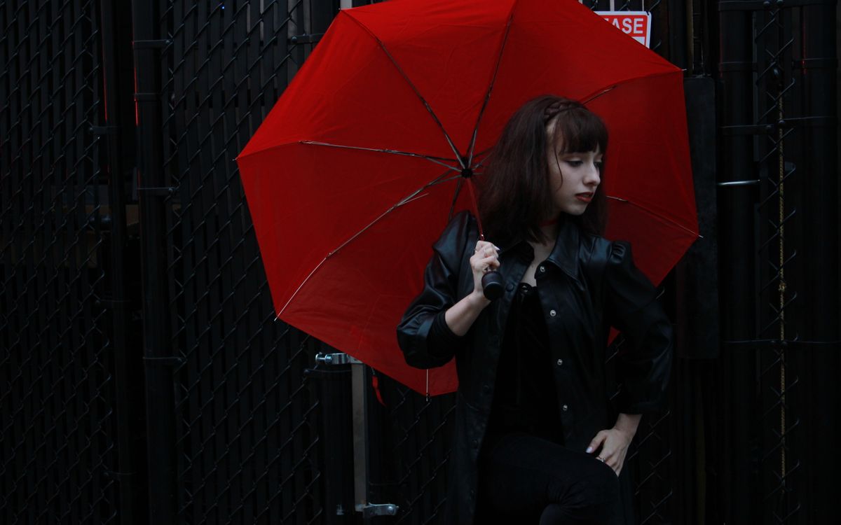 Femme caucasienne en veste de cuir noire avec un parapluie rouge en extérieur