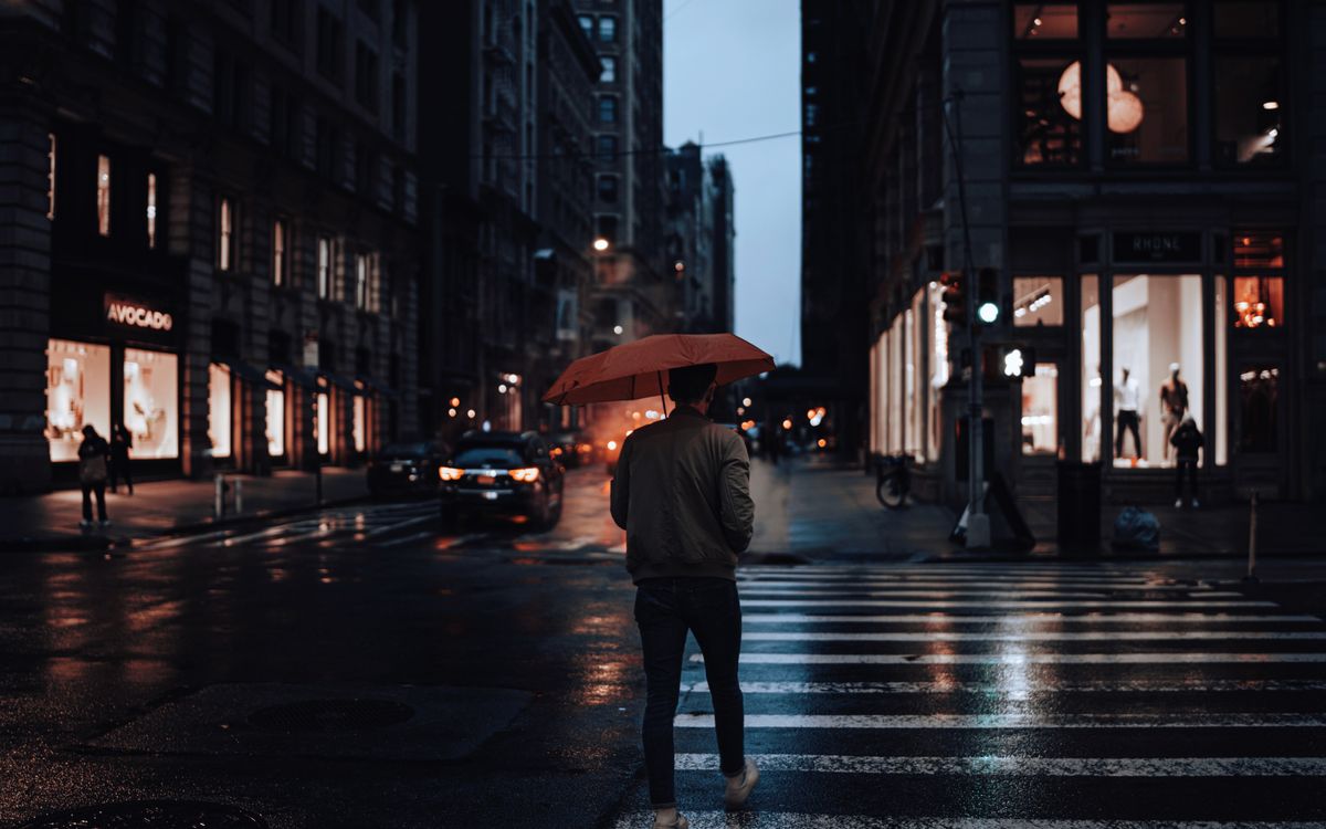 Homme marchant avec un parapluie rouge dans une rue de ville sous la pluie la nuit