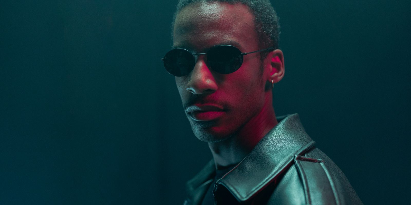 Buneri.fr | Une veste en cuir véritable vaut-elle vraiment son prix ? Portrait stylisé d'un homme en lunettes de soleil et veste en cuir dans une ambiance dramatique