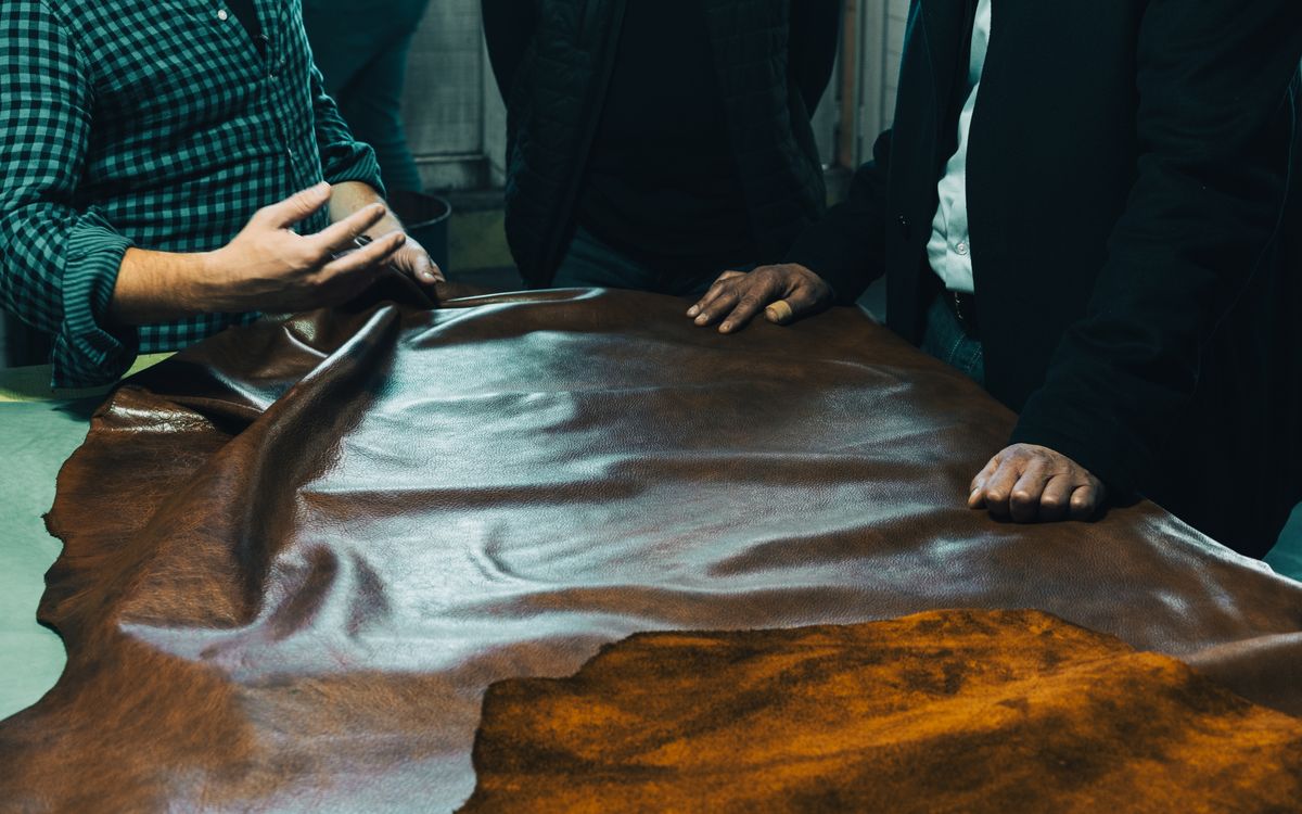 Buneri.fr | Une veste en cuir véritable vaut-elle vraiment son prix ? Groupe d'artisans examinant du cuir sur une table, attentifs à la qualité et au choix de la matière