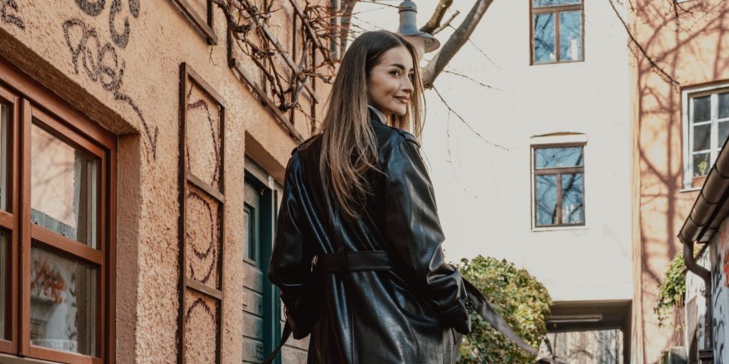 Femme elegante en long manteau de cuir noir marchant dans une rue couverte de graffitis