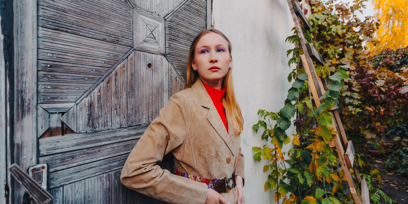 Femme en veste de daim fauve appuyee contre une vieille porte patinee dans la lumiere d automne