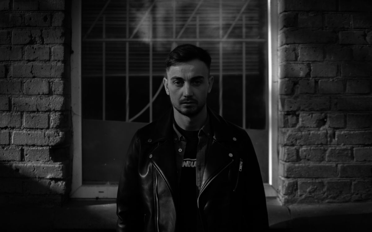 Portrait en noir et blanc d'un homme adulte en blouson de cuir devant un mur de briques