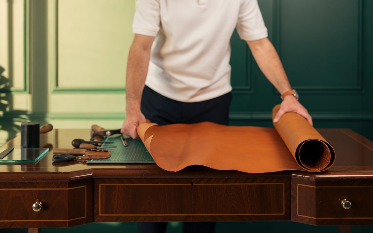 Artisan préparant une pièce de cuir sur un établi avec des outils traditionnels