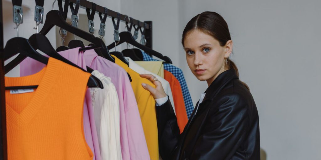 Femme élégante en veste de cuir noire parcourant des vêtements sur un portant dans une boutique lumineuse
