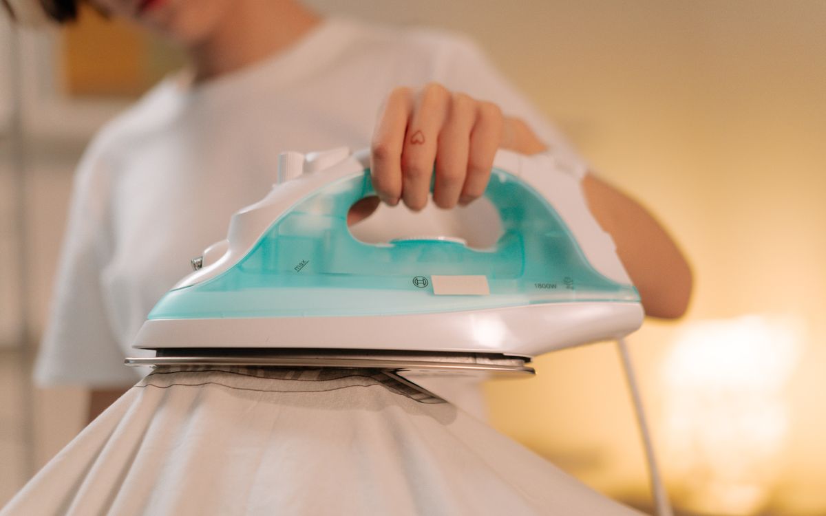 Gros plan d'une personne lissant un vêtement clair avec un fer à vapeur en intérieur