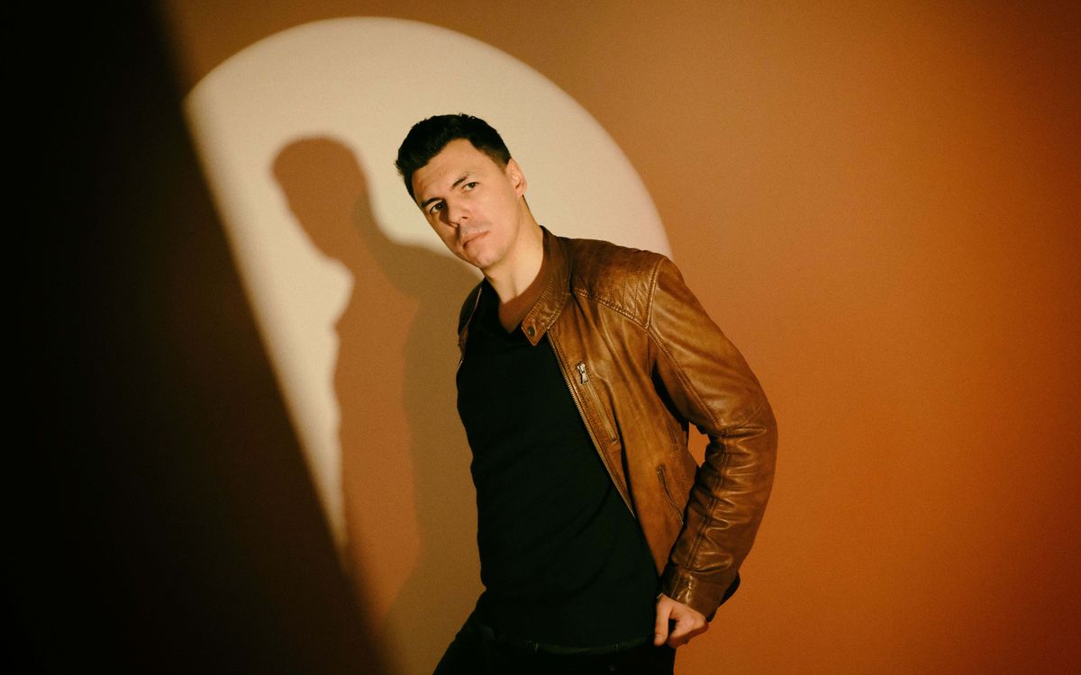 Un homme élégant en blouson de cuir marron pose avec assurance dans un studio