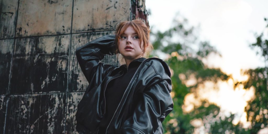 Jeune femme élégante en veste de cuir posant en extérieur devant un décor urbain