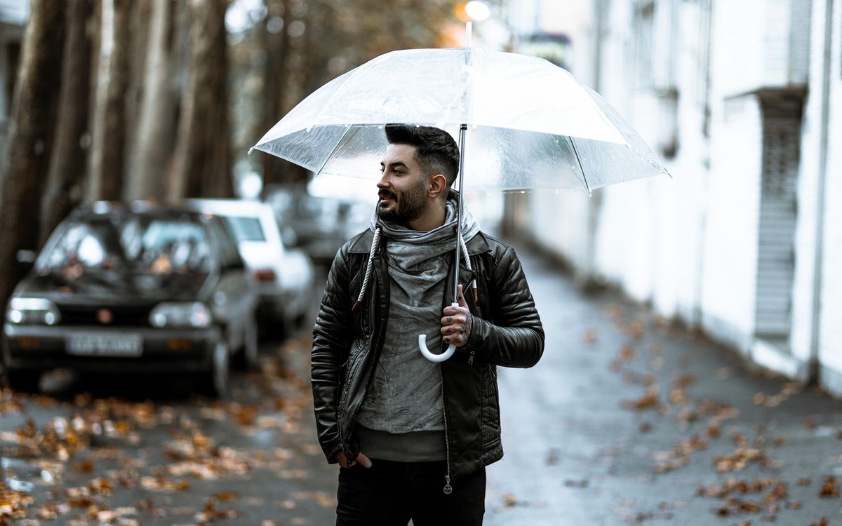 Homme confiant tenant un parapluie transparent dans une rue de ville sous la pluie