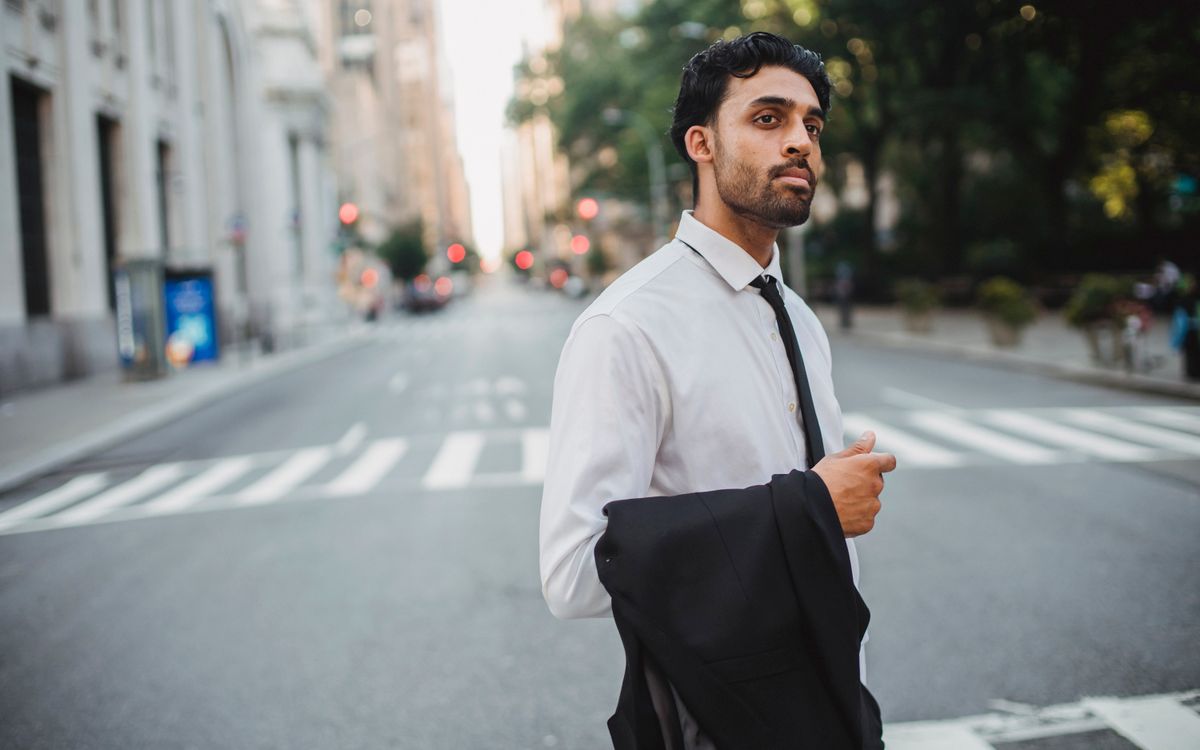 Un homme d'affaires confiant traverse une rue en tenant sa veste de costume par une belle journée