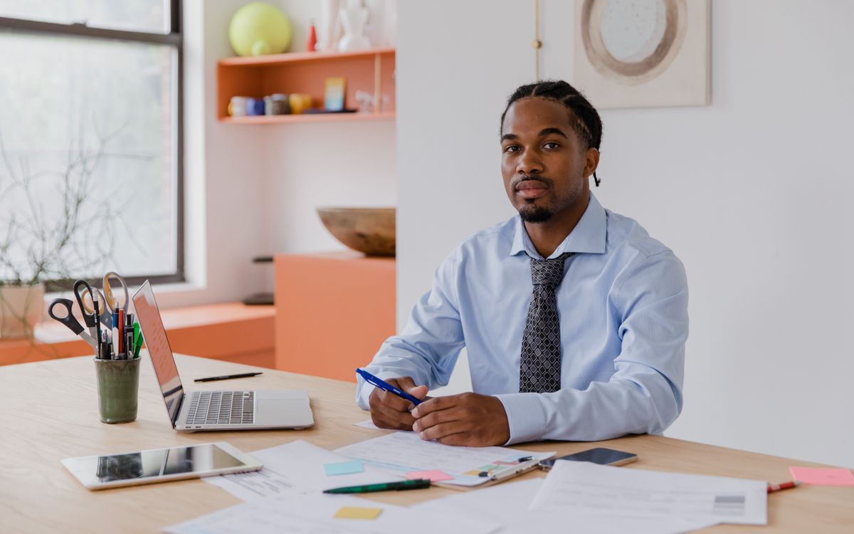 Un homme d'affaires professionnel avec une barbe et des cheveux tressés est assis à son bureau avec un ordinateur portable et des documents
