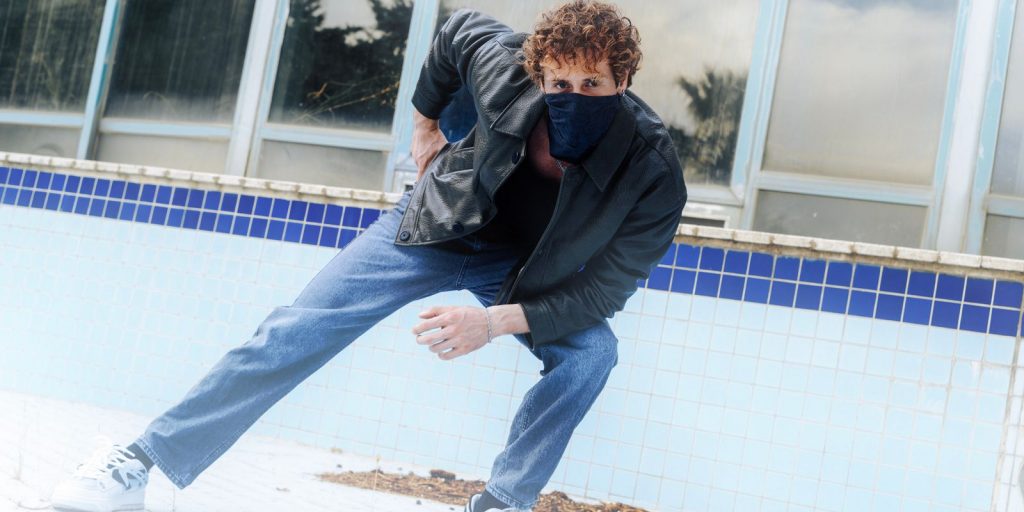 Homme en veste de cuir et jean adossé à un mur dans une pose stylée et détendue