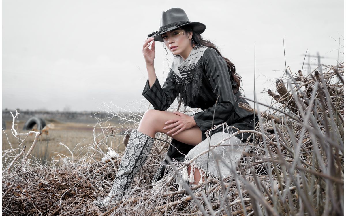 Femme élégante en tenue western posant en extérieur dans un champ rural aux herbes sèches