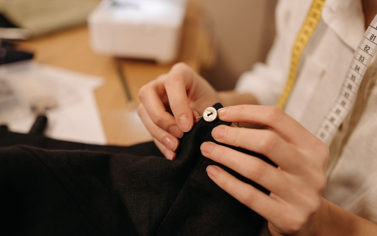 Gros plan sur les mains d'un tailleur cousant un bouton avec une aiguille et du fil