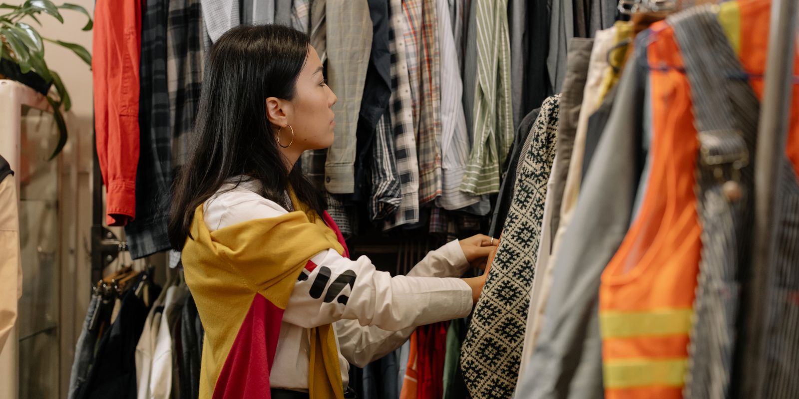 Une jeune femme parcourt un portant de vêtements dans une friperie pleine de tenues colorées
