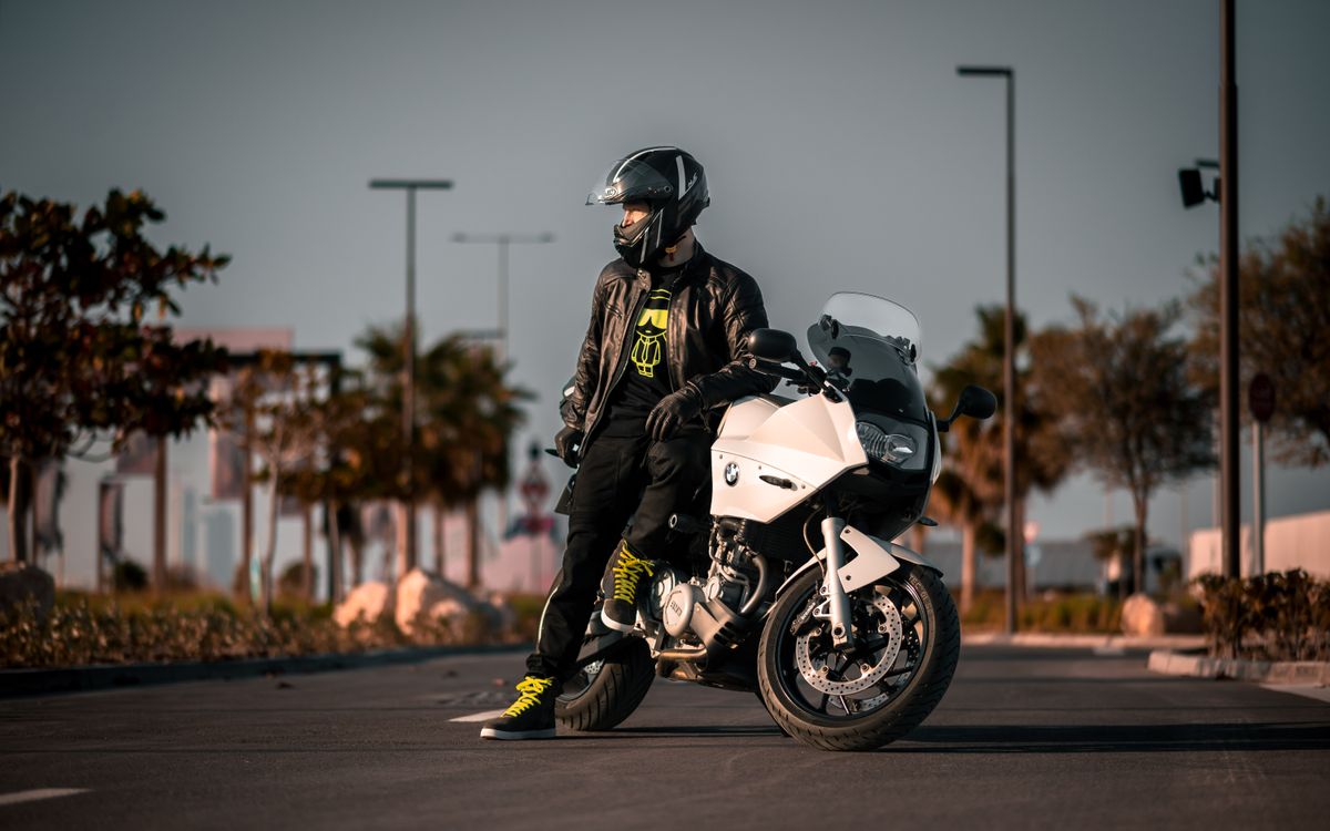 Un motard en tenue noire se tient près de sa moto en plein jour