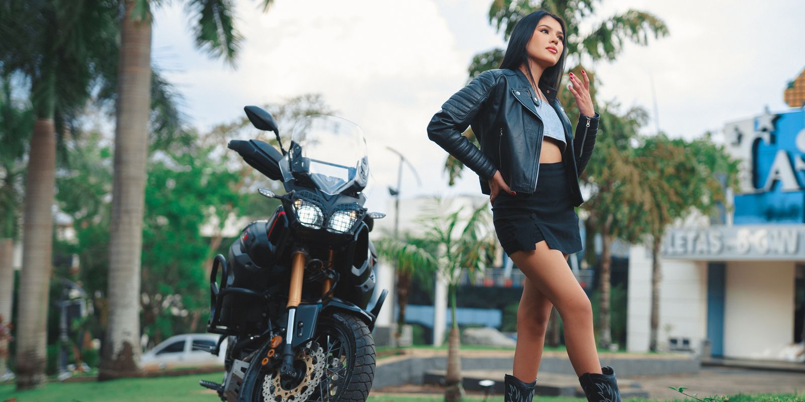 Femme sûre d'elle en veste de motard en cuir devant une moto au soleil