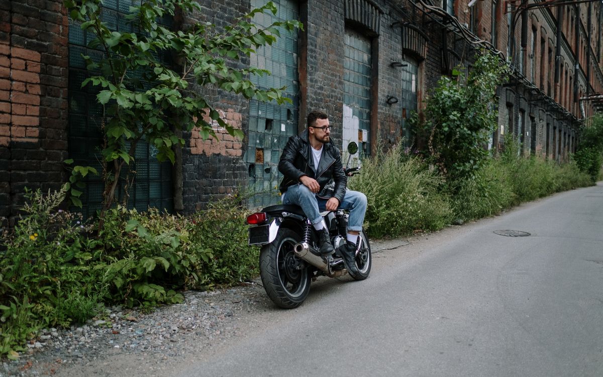 Homme en veste en cuir assis sur une moto dans un cadre urbain