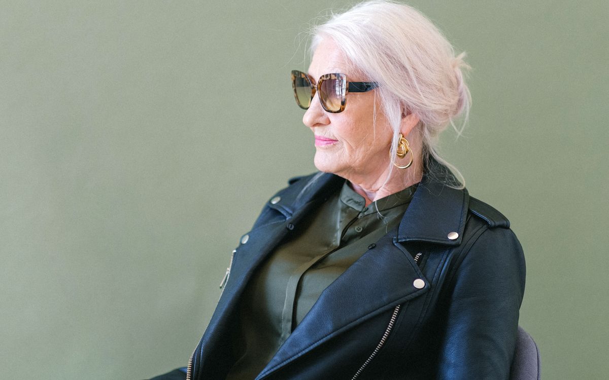 Femme confiante en veste de cuir élégante et lunettes de soleil devant un fond vert