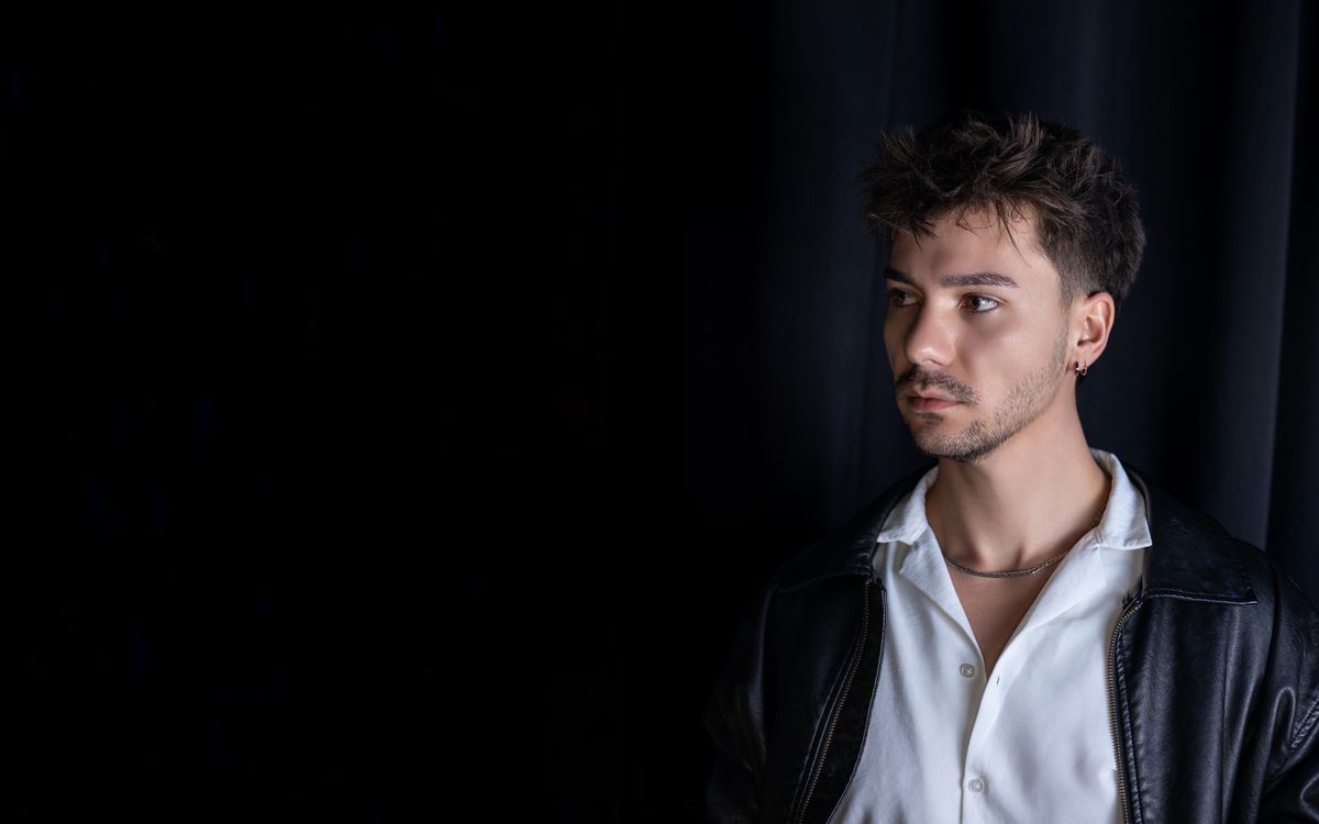 Homme en veste en cuir posant à l'intérieur devant un rideau noir