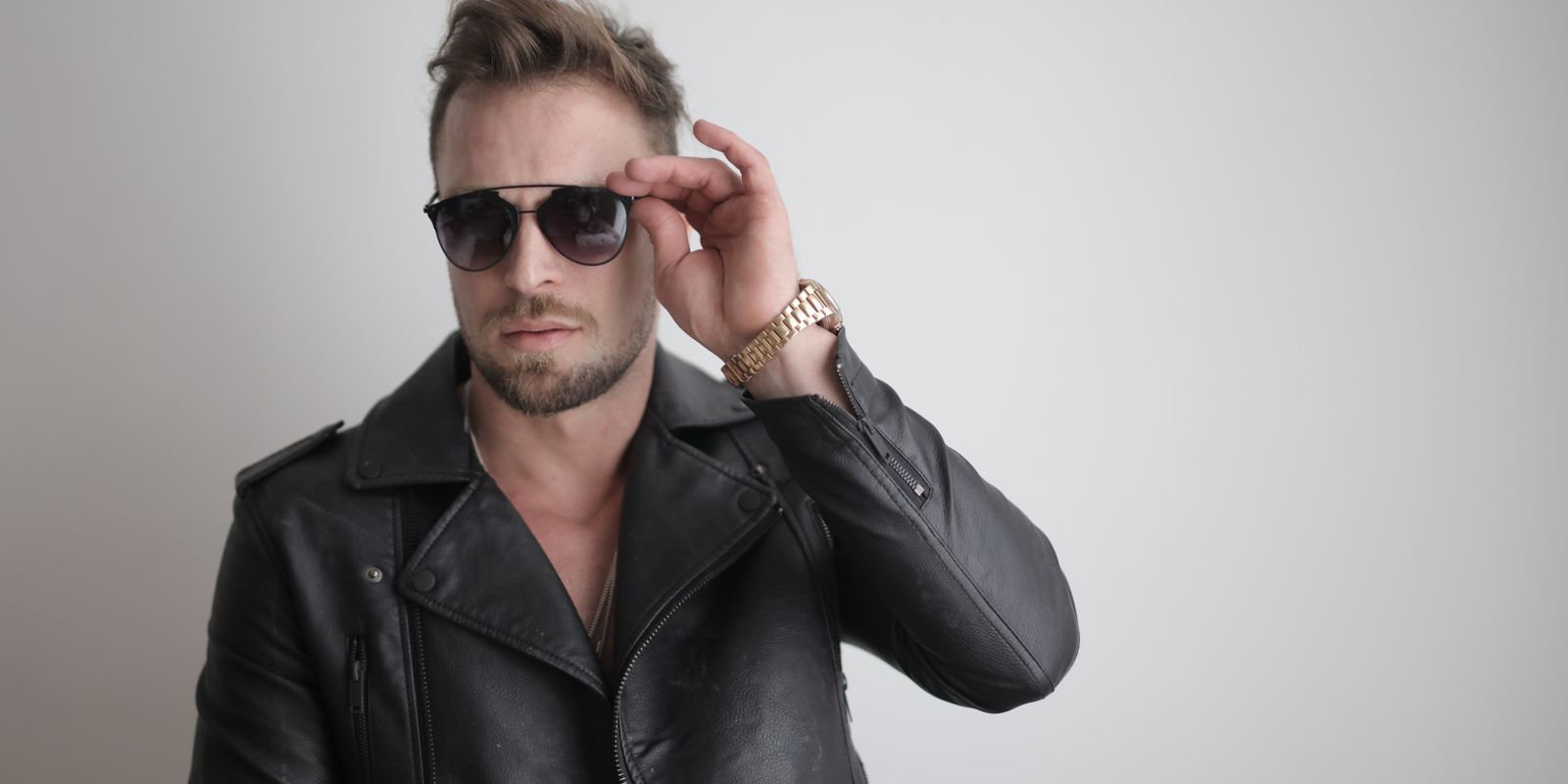 Homme élégant en veste de cuir noire et lunettes de soleil posant en intérieur