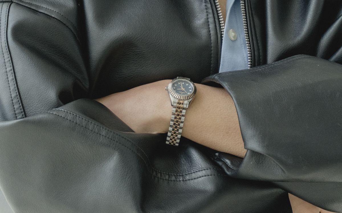 Gros plan d'une montre portée sur la manche d'une veste en cuir, montrant le grain et les coutures