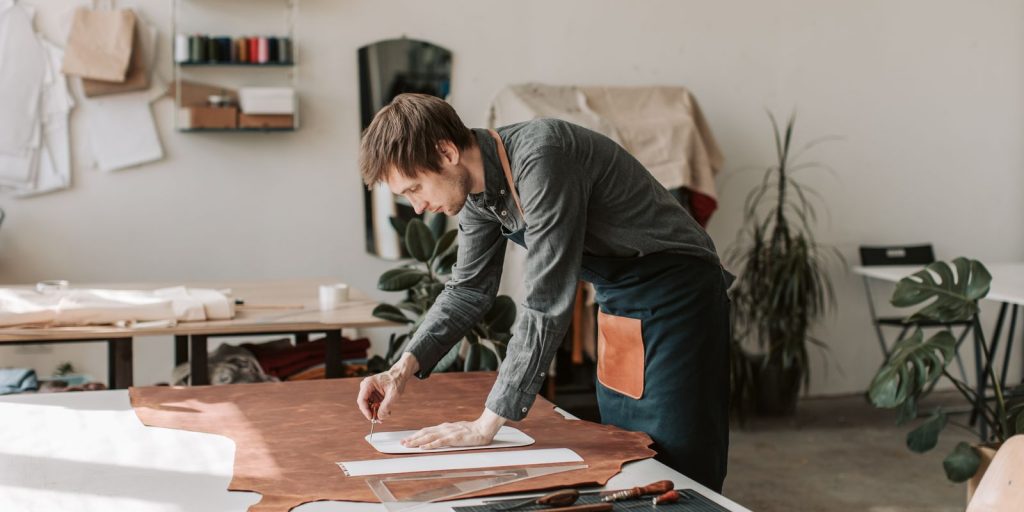 Un artisan dessine et découpe du cuir dans un atelier ensoleillé, illustrant un savoir-faire fait main