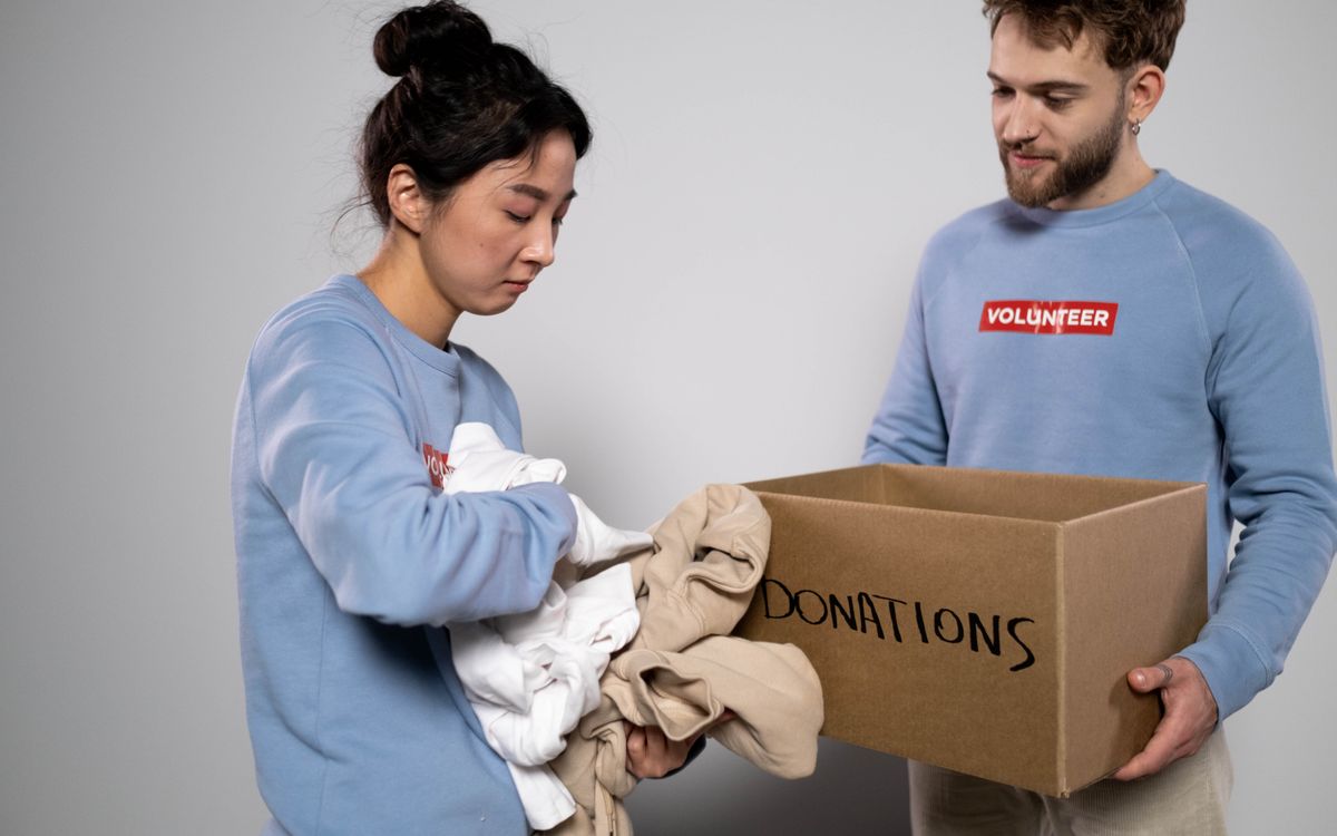 Deux bénévoles rangent des vêtements dans une boîte de dons, illustrant l'entraide et la générosité