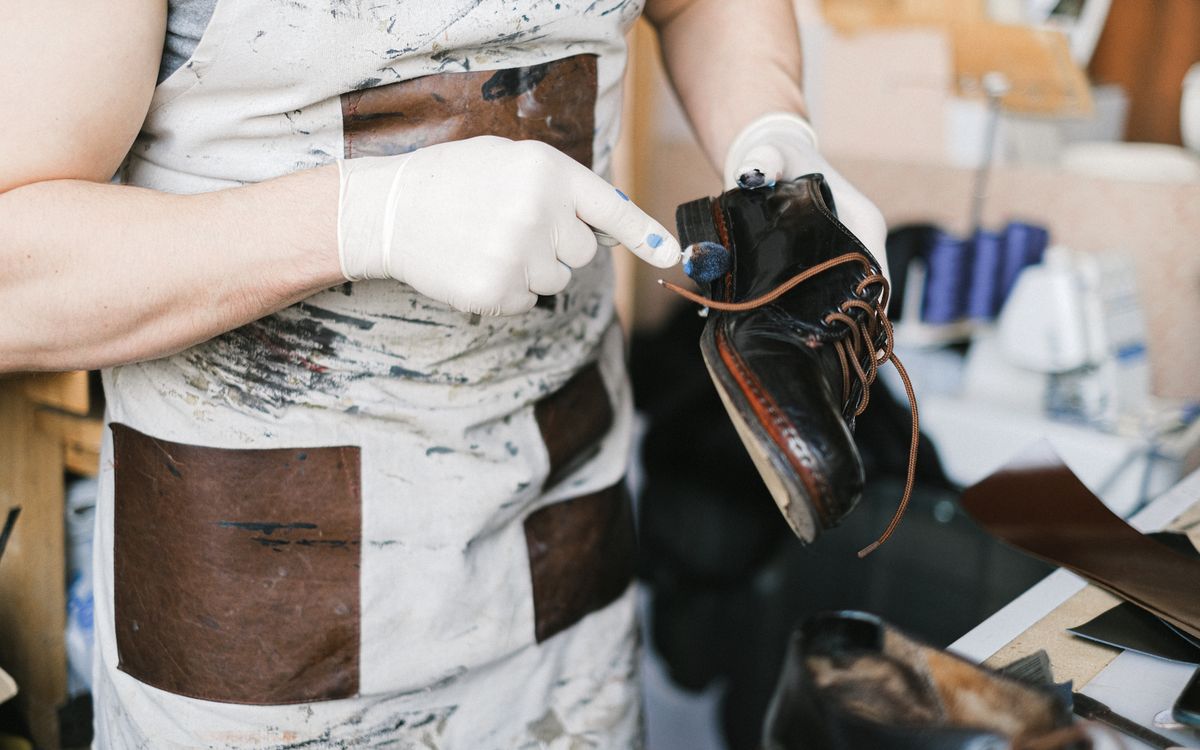 Un artisan ganté fait pénétrer un soin nourrissant dans le cuir en atelier, restaurant sa finition