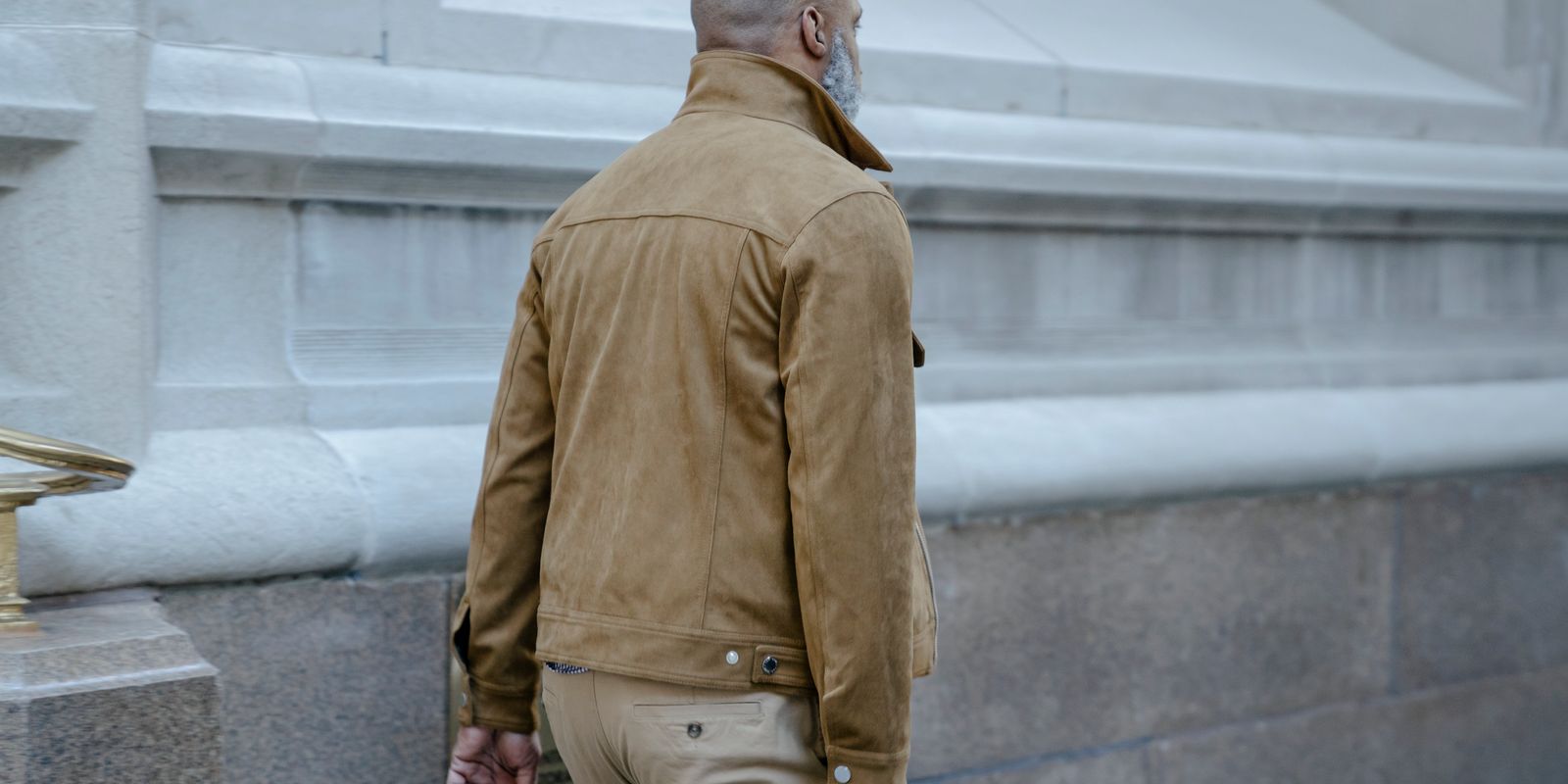 Homme portant une élégante veste en cuir marron devant un bâtiment classique