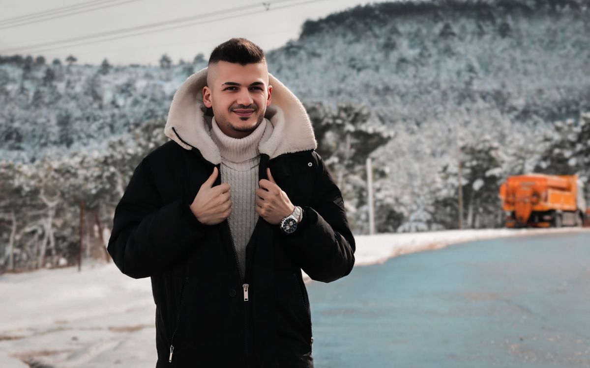 Un jeune homme en tenue d'hiver devant une forêt enneigée