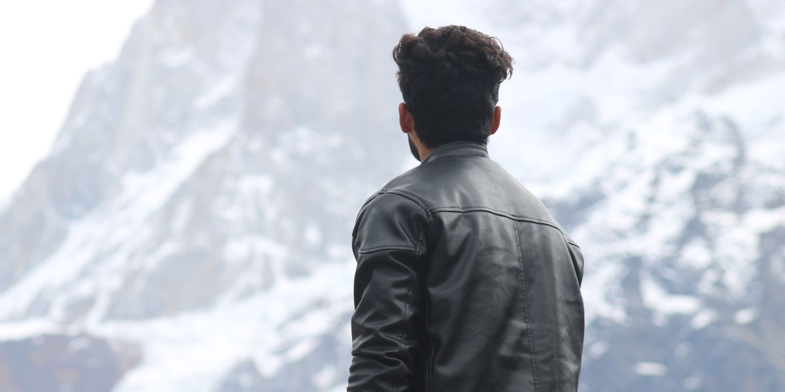 Un homme en veste de cuir contemplant des montagnes enneigées sous un ciel d'hiver dégagé