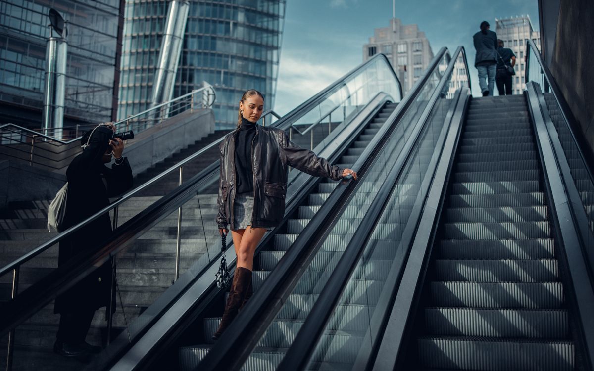 Une femme élégante pose sur un escalator urbain en veste en cuir pour un shooting mode moderne