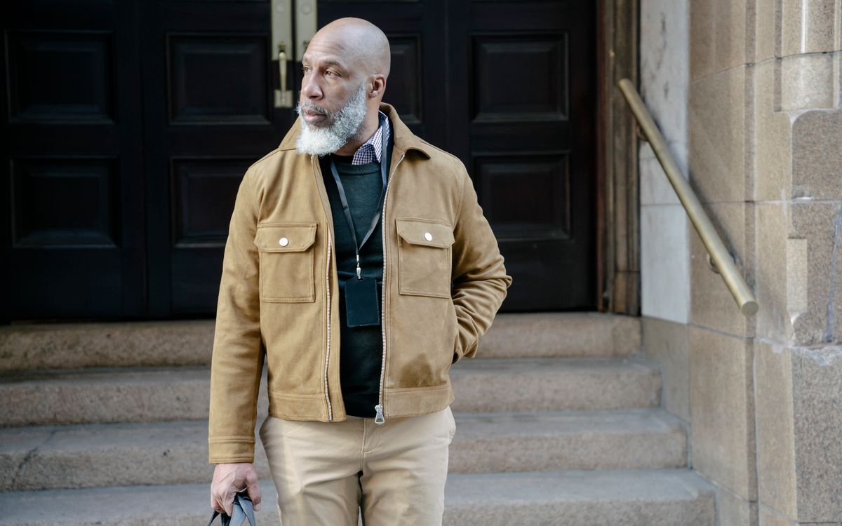 Un homme barbu en veste marron élégante en extérieur, près d'un escalier, à la finition douce et mate