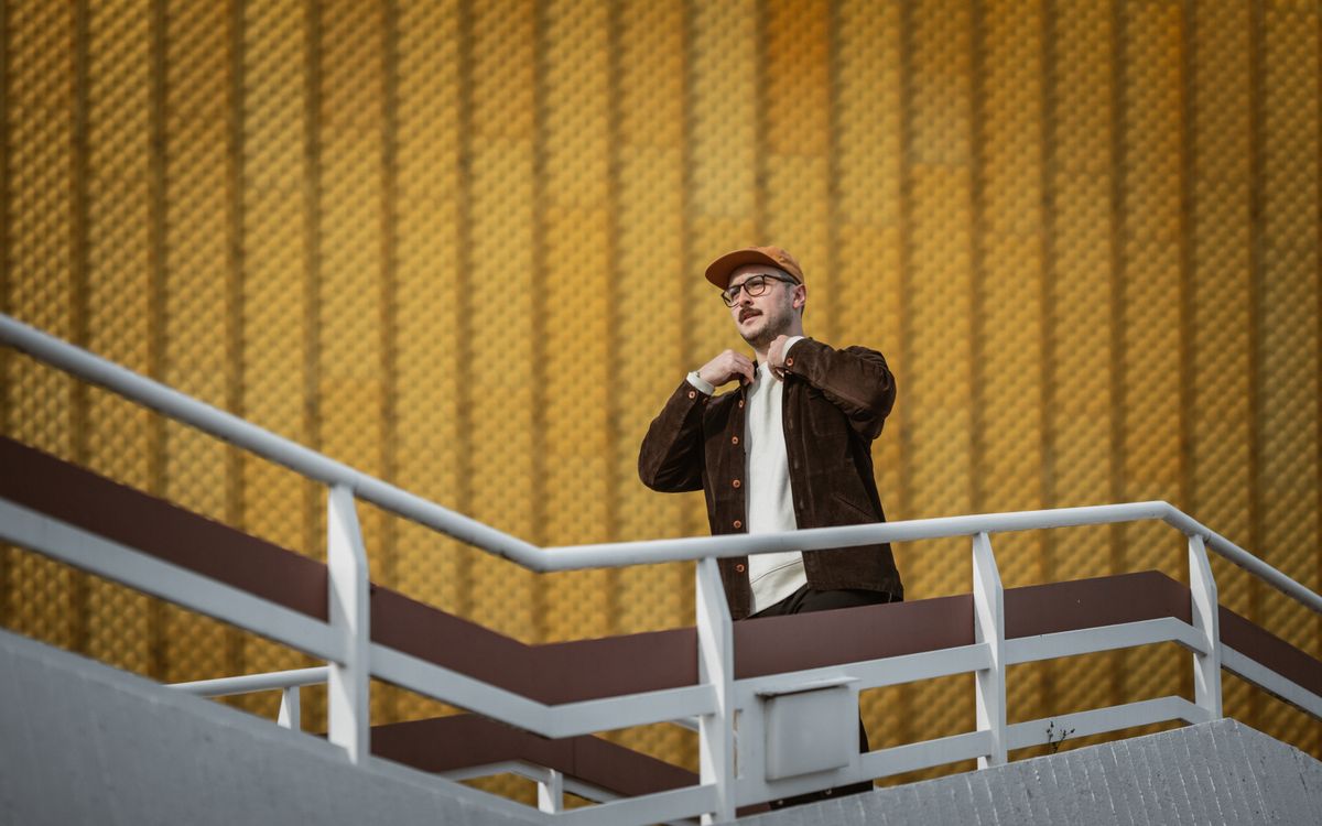 Un homme élégant en tenue urbaine se tient sur un escalier contemporain devant un mur texturé