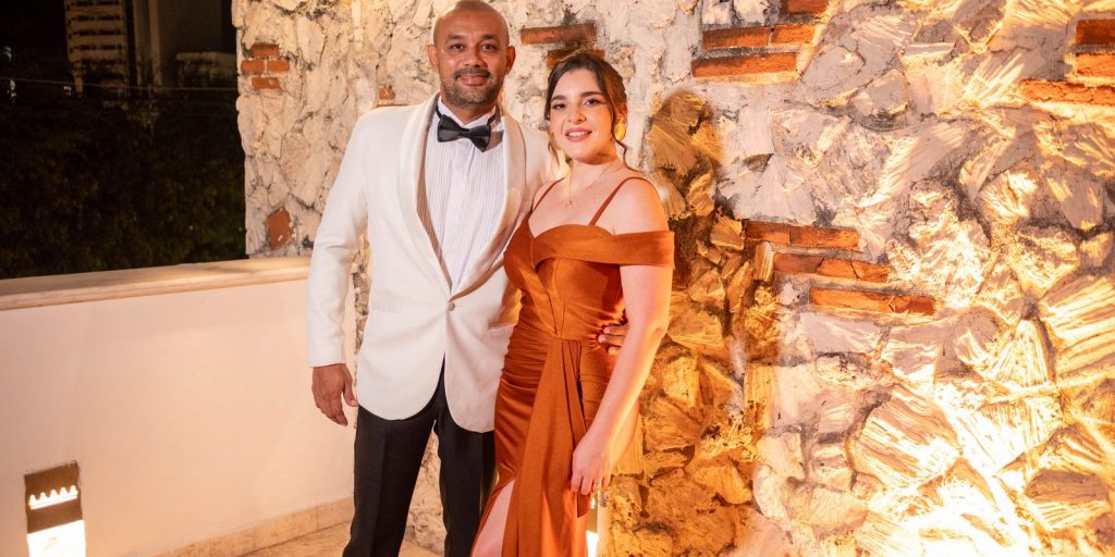 Couple élégant en tenue de soirée posant ensemble devant un mur de pierre illuminé